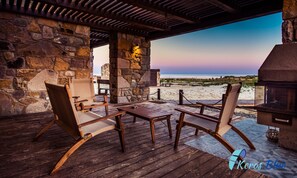 A wooden deck with stone walls, outdoor seating, and a view of the beach. - Keros Blue (Lemnos)