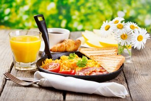 A breakfast setting with scrambled eggs, bacon, toast, and a glass of orange juice on a wooden table. - Keros Blue (Lemnos)