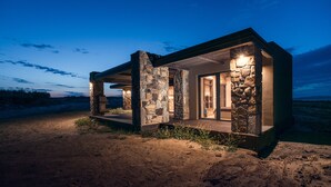 A stone cabin with a covered porch and a single visible room with a door and windows. - Keros Blue (Lemnos)