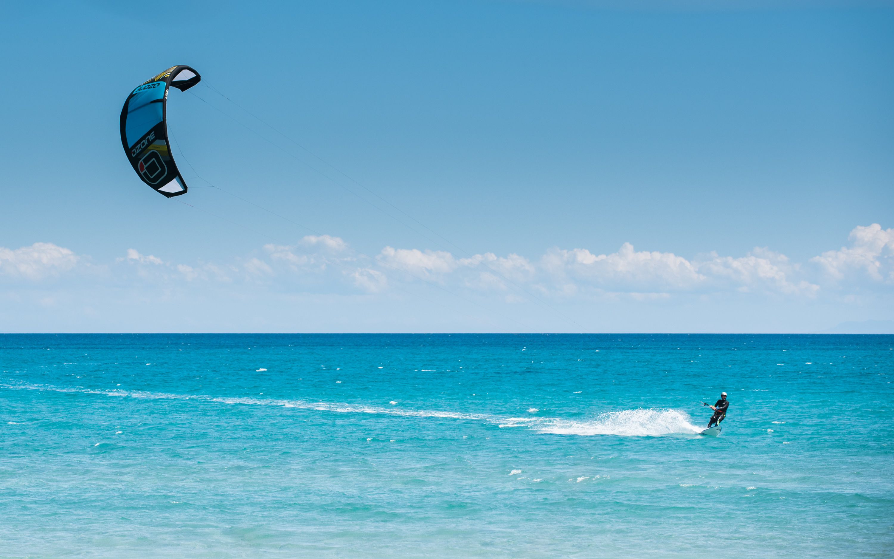 En person kitesurfer på et klart, blå hav med en drage i himlen.