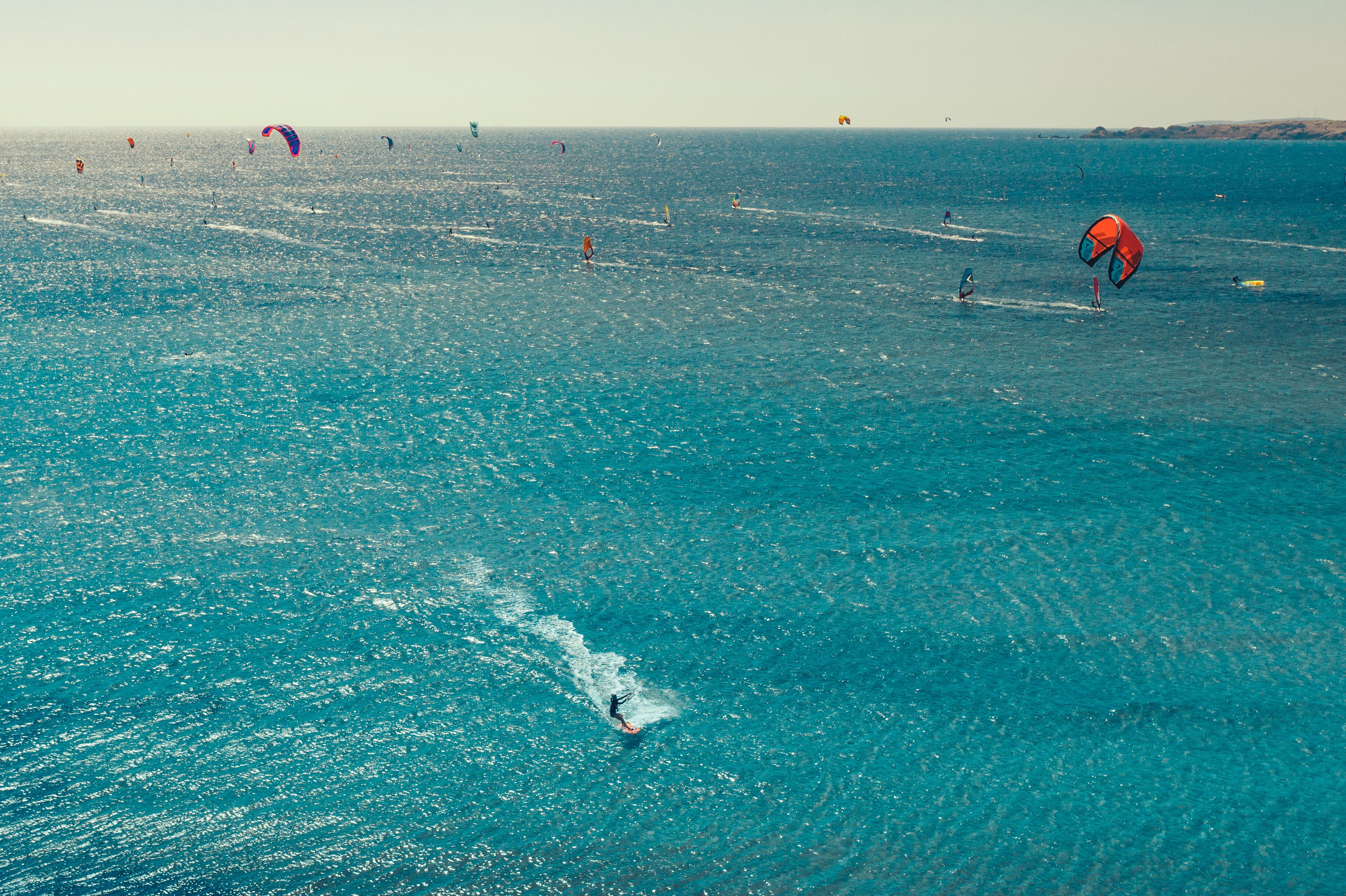Zona costera con aguas azul turquesa y varios windsurfistas.