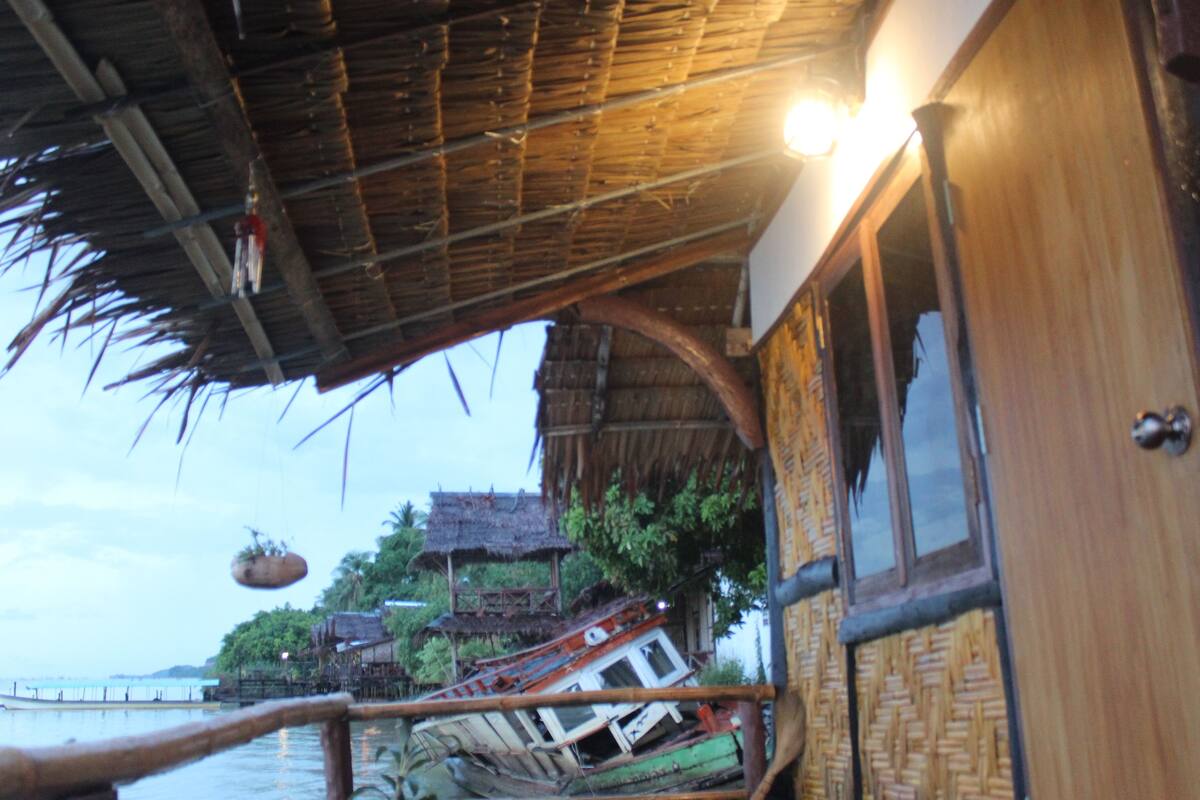 A traditional wooden house with a thatched roof, a wooden balcony, and a view of the water.