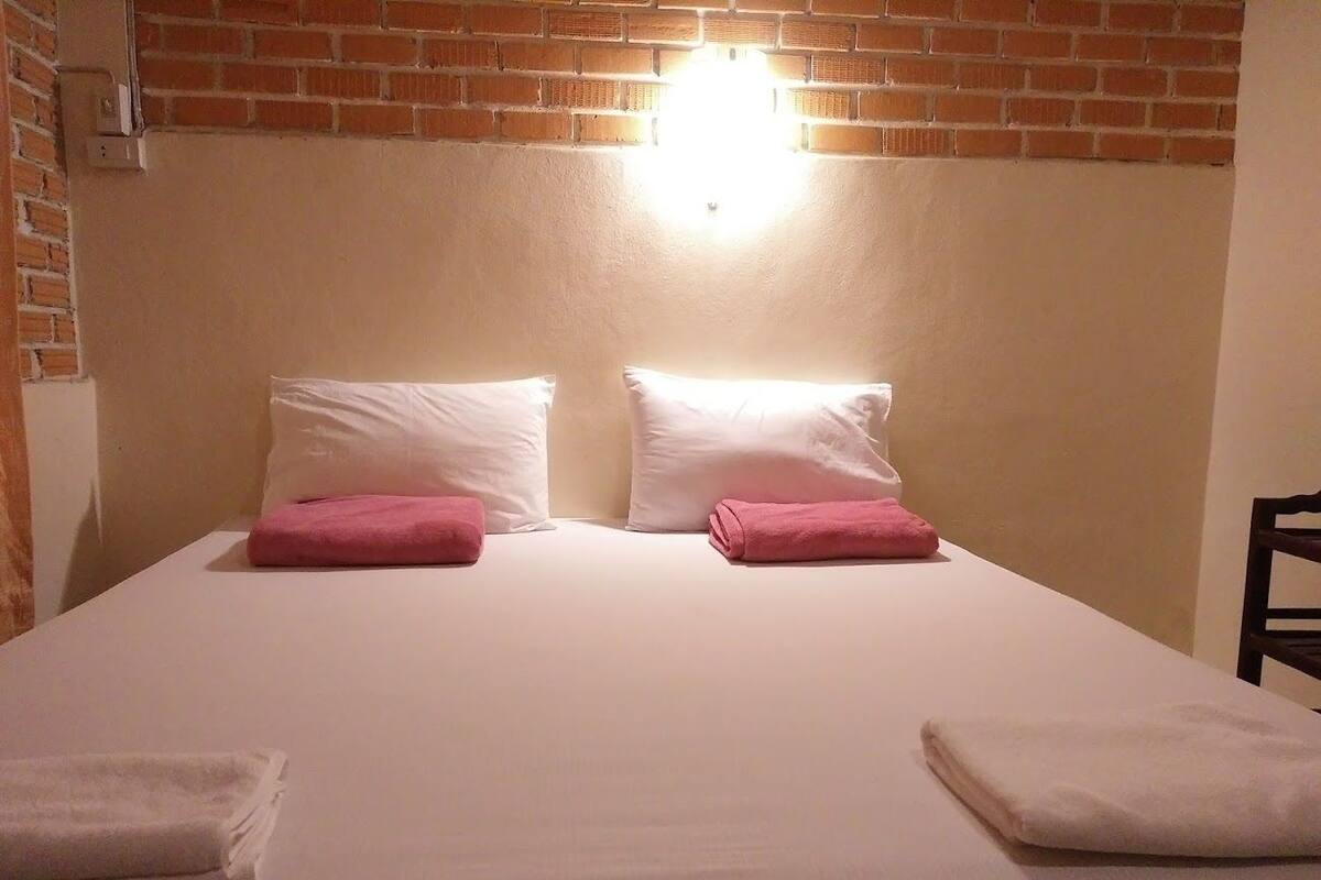 A bed with white linens, two pink towels, and a wall-mounted light fixture.