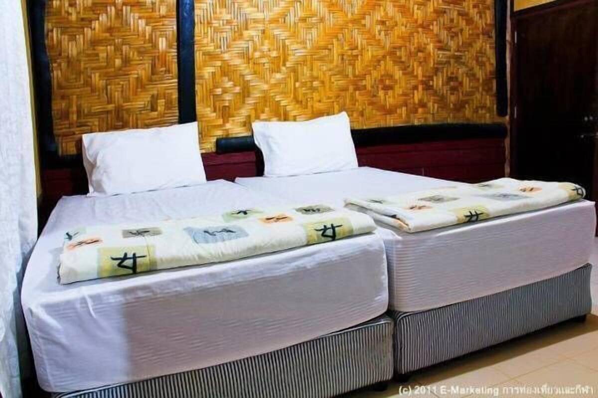A double bed with white bedding and a patterned blanket, set against a woven wall.