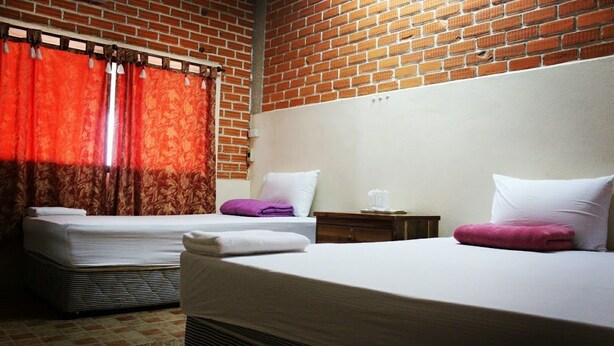 A hotel room with two beds, red curtains, a brick wall, and a white headboard. - Khaochan Resort (Pak Phayun)