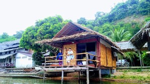 A wooden house with a thatched roof on stilts over water, surrounded by lush greenery. - Khaochan Resort (Pak Phayun)