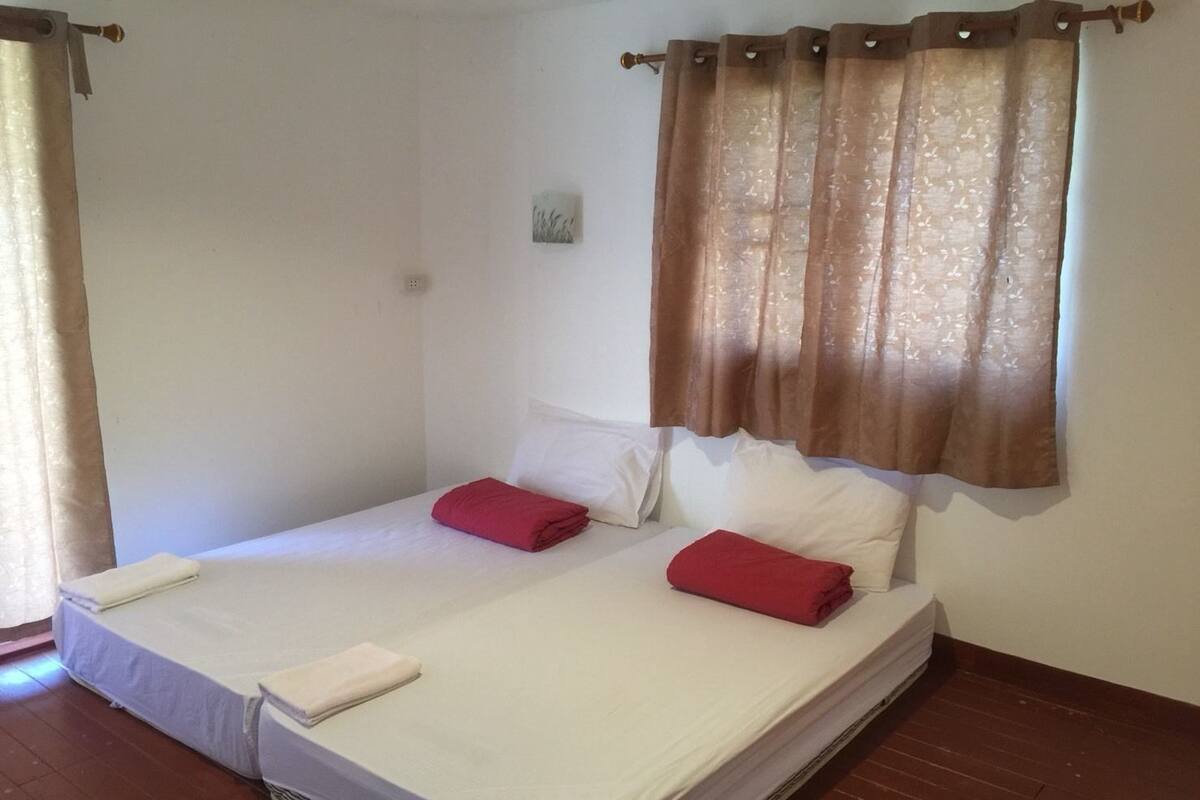A double bed with white linens and red towels, a brown curtain, and a small picture on the wall.