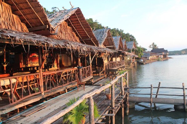 A row of thatched-roof overwater bungalows with wooden walkways over calm water. - Khaochan Resort (Pak Phayun)