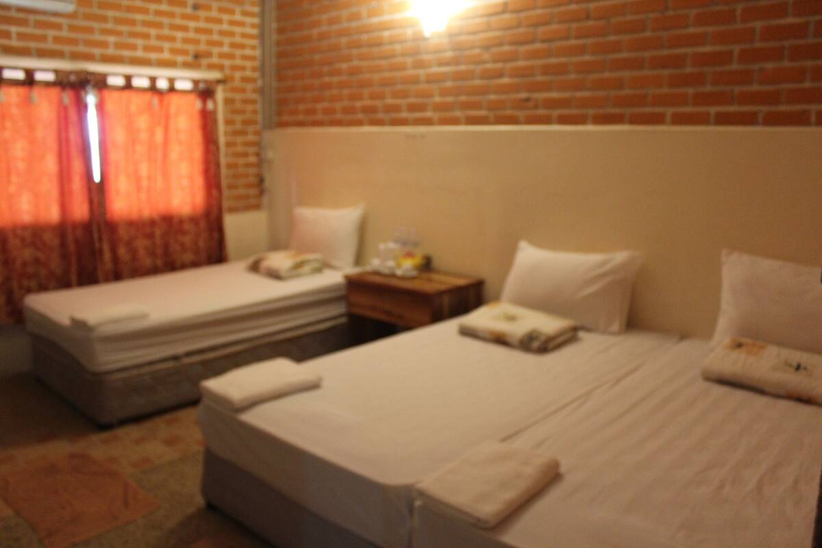 A hotel room with two beds, a brick wall, and a window with curtains.