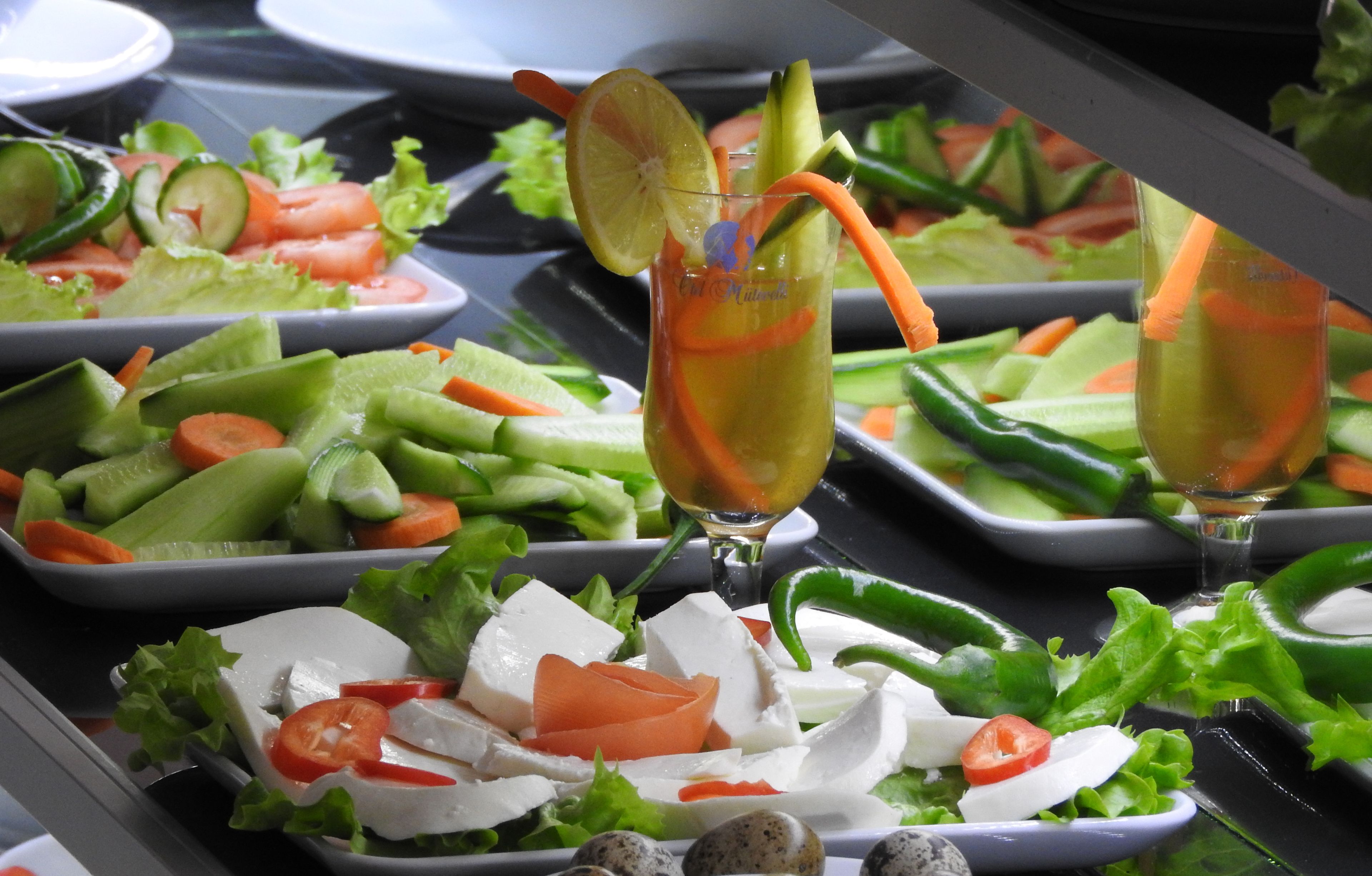 A buffet with various salads and a drink with a lemon slice and carrot.