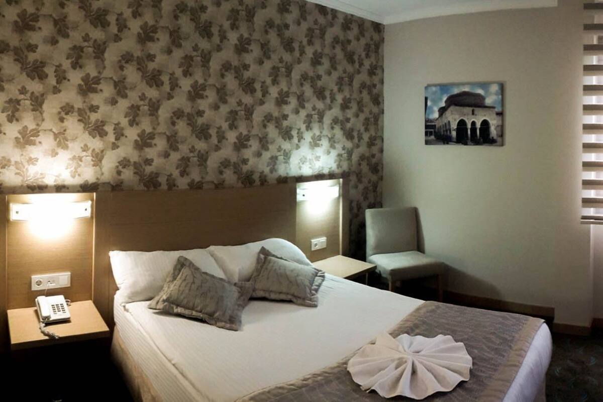 A hotel room with a bed, bedside table, chair, desk, mirror, and a wall-mounted picture.