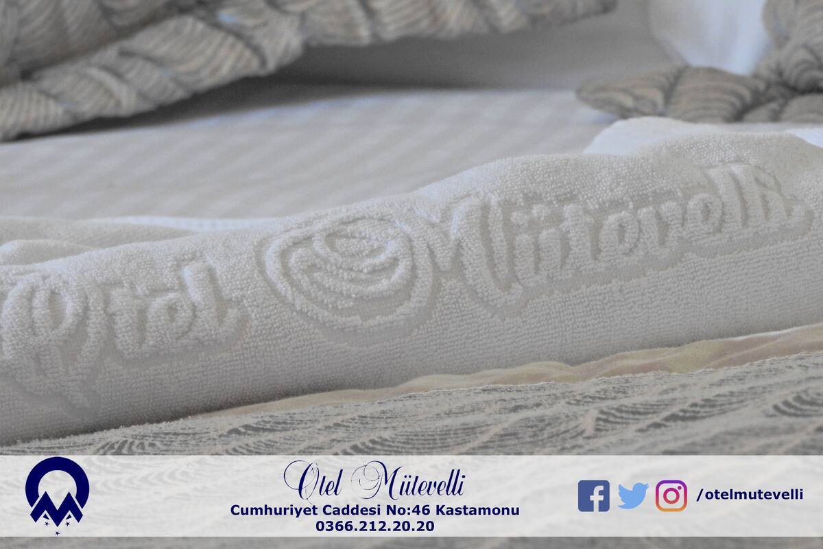 A close-up of a white bedspread with a textured pattern and the name "Otel Mielevelli" embroidered on it.
