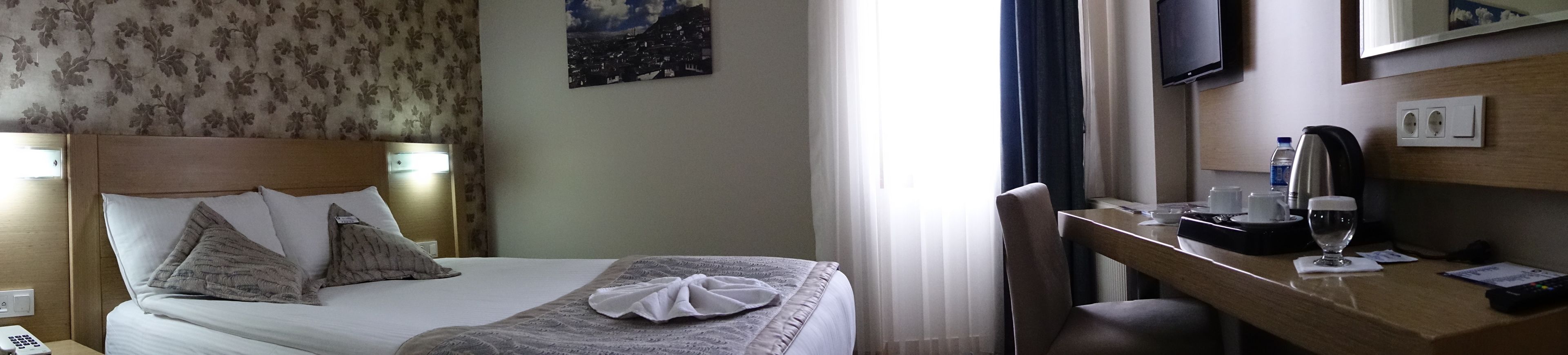 A hotel room with a bed, a desk, a chair, a TV, and a window with curtains.