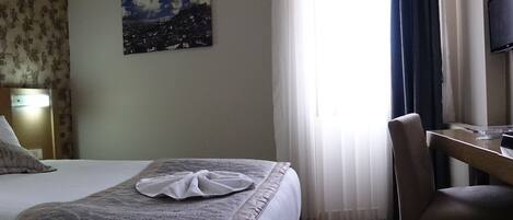 A hotel room with a bed, a desk, a chair, a TV, and a window with curtains.