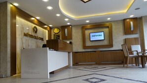 Ein Hotel-Empfangsbereich mit Empfangstresen, einem Bildschirm, der 'KASTAMONU' anzeigt, und einer Sitzecke mit Stühlen.