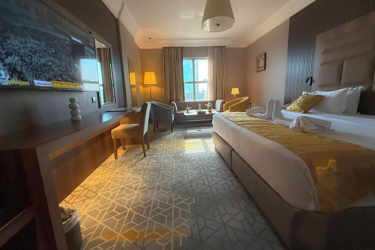 A hotel room with a bed, a desk, a chair, a TV, and a window with curtains.