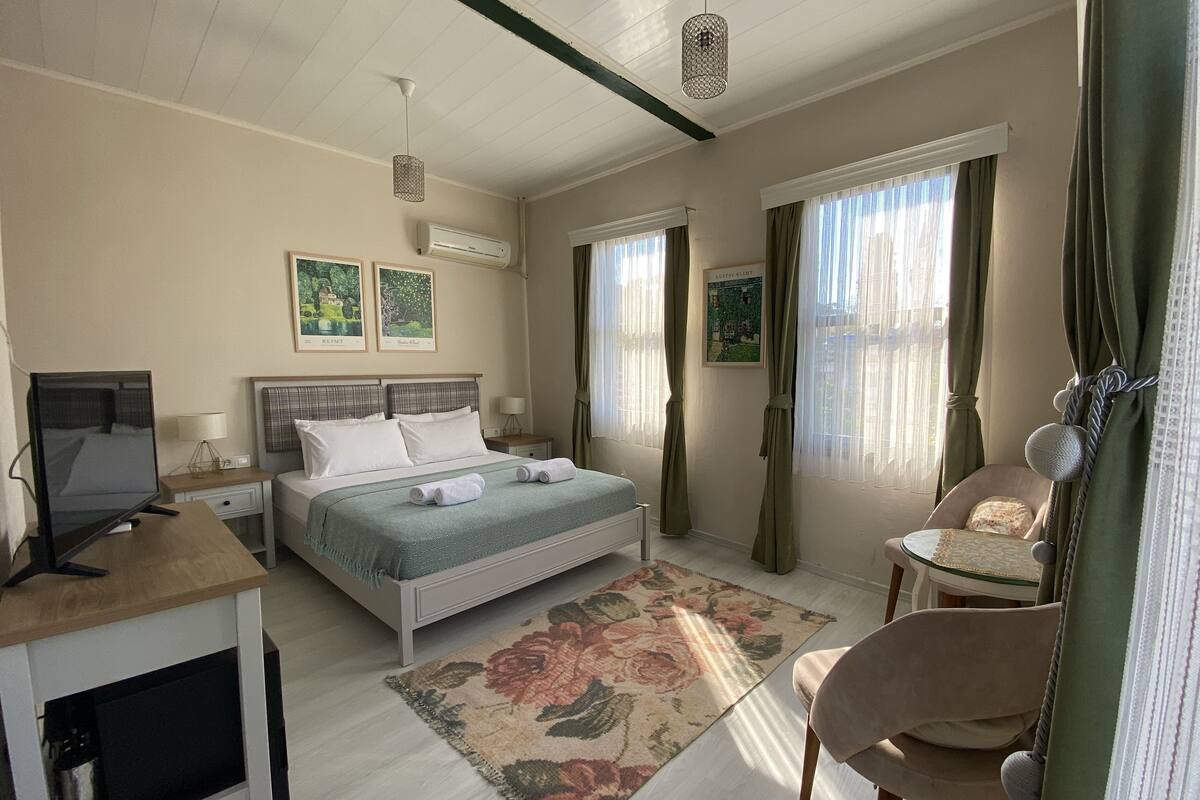A hotel room with a bed, a desk with a computer, a chair, and a window with curtains.