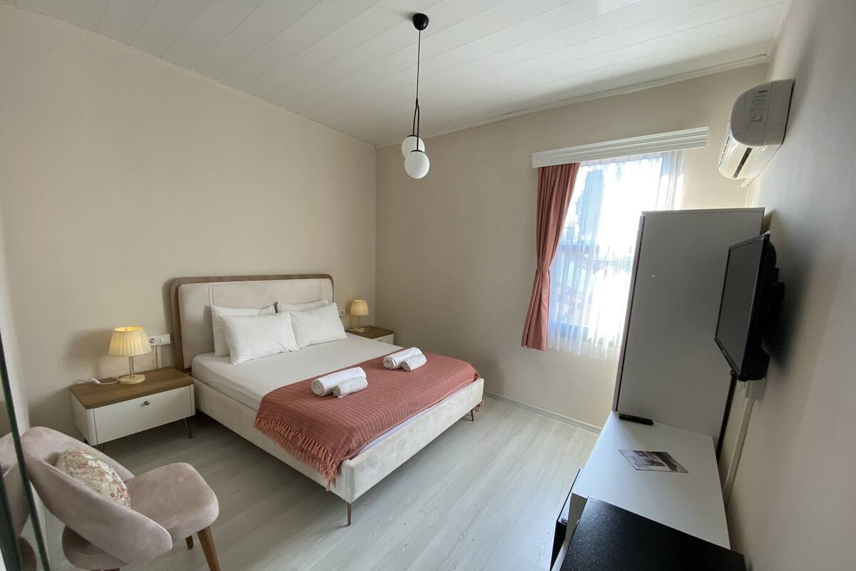 A hotel room with a bed, bedside lamps, a chair, a desk with a computer, and a TV.