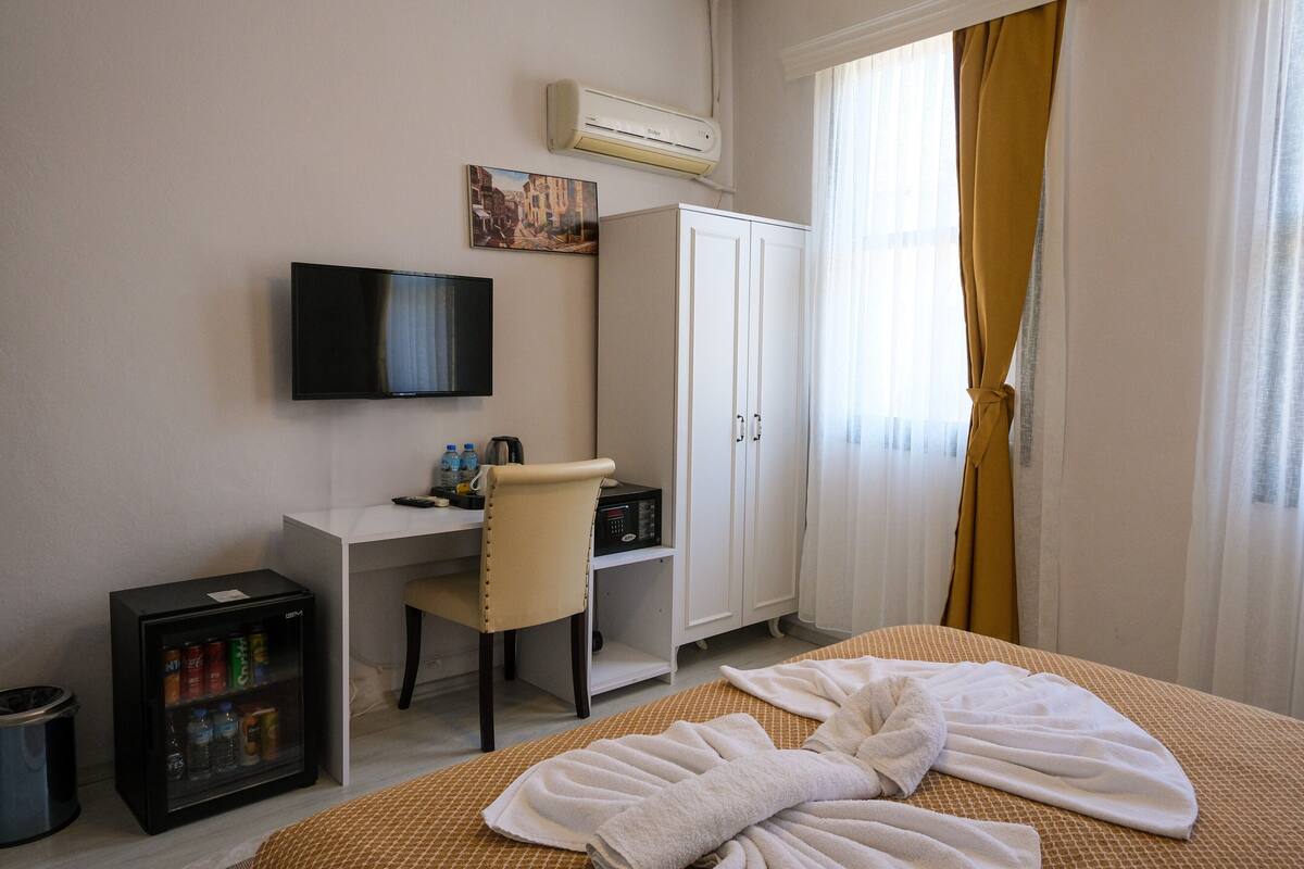 A hotel room with a bed, a desk with a chair, a television, a wardrobe, and a minibar.