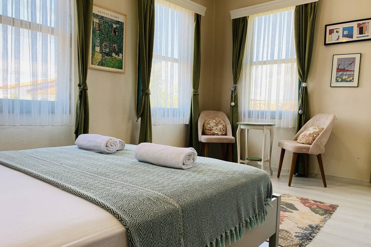 A hotel room with a bed, two chairs, a small table, and a window with curtains.