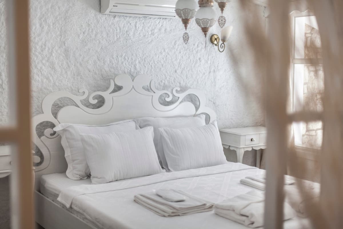 A neatly made bed with white linens, a decorative headboard, and a bedside table with a lamp.
