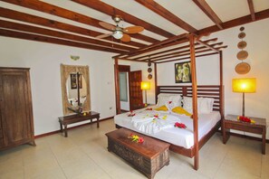 A four-poster bed with a canopy, a wooden bench, a bedside table, and a mirror on the wall.