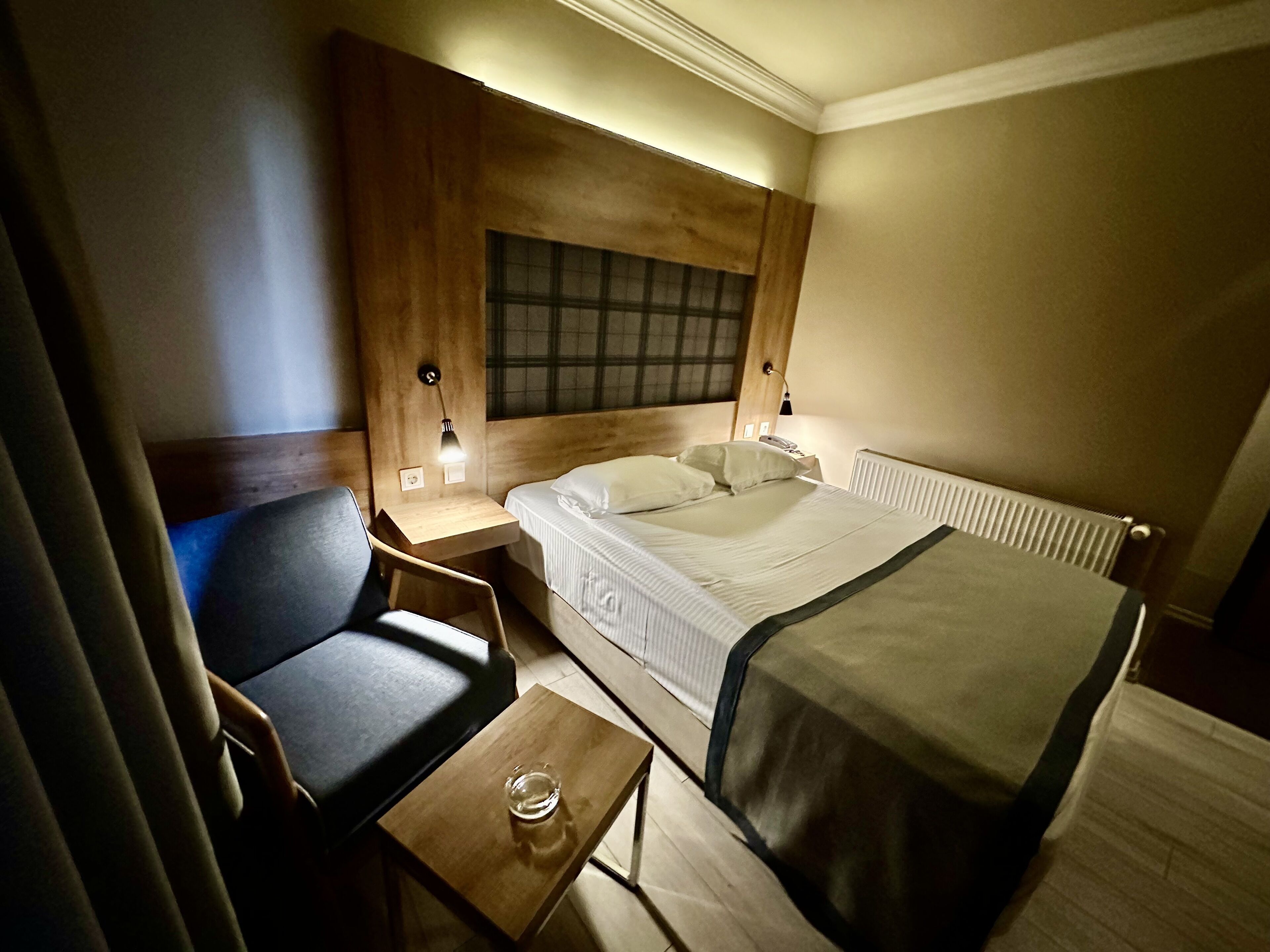 Una habitación de hotel con cama, mesita de noche, silla y una pequeña mesa con un vaso.