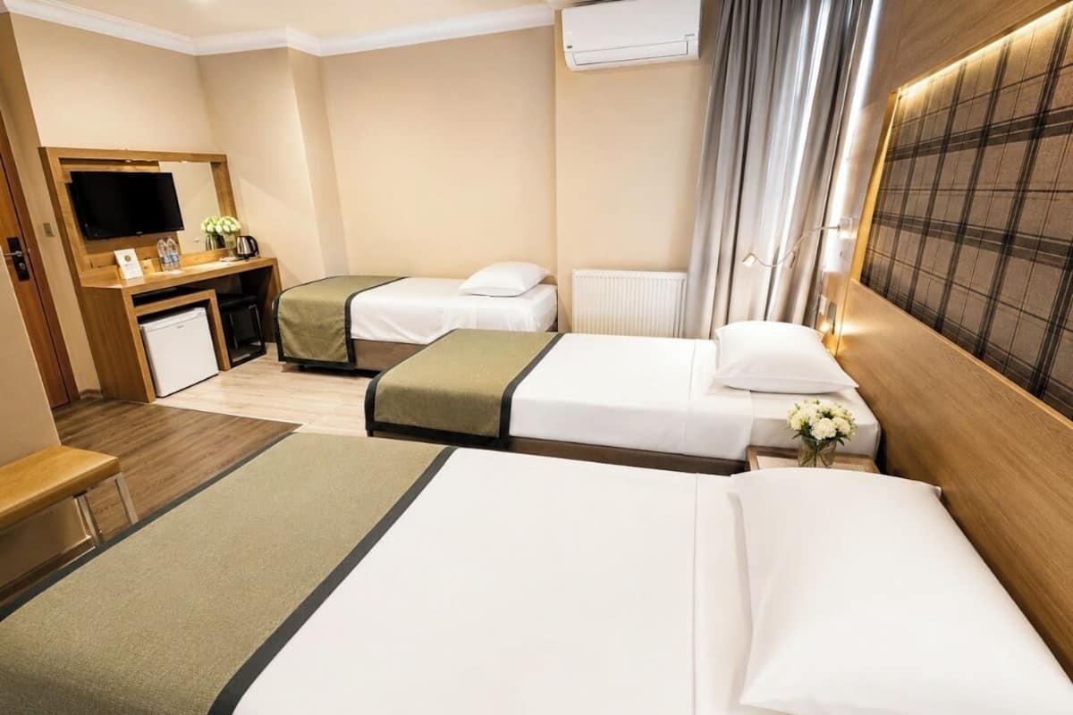 A hotel room with two beds, a desk with a TV, a small fridge, and a window with curtains.