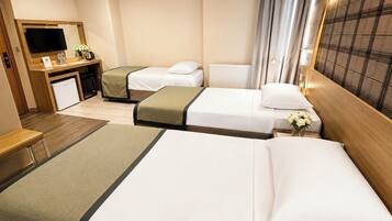 A hotel room with two beds, a desk with a TV, a small fridge, and a window with curtains.