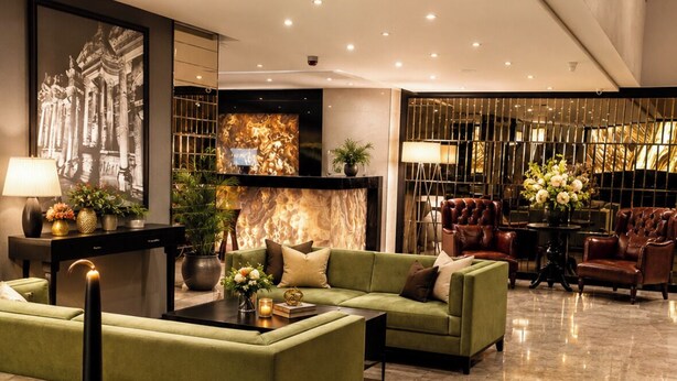 A modern lobby with a green sofa, a coffee table, and a decorative vase with flowers. - Laodikya Otel (Denizli)