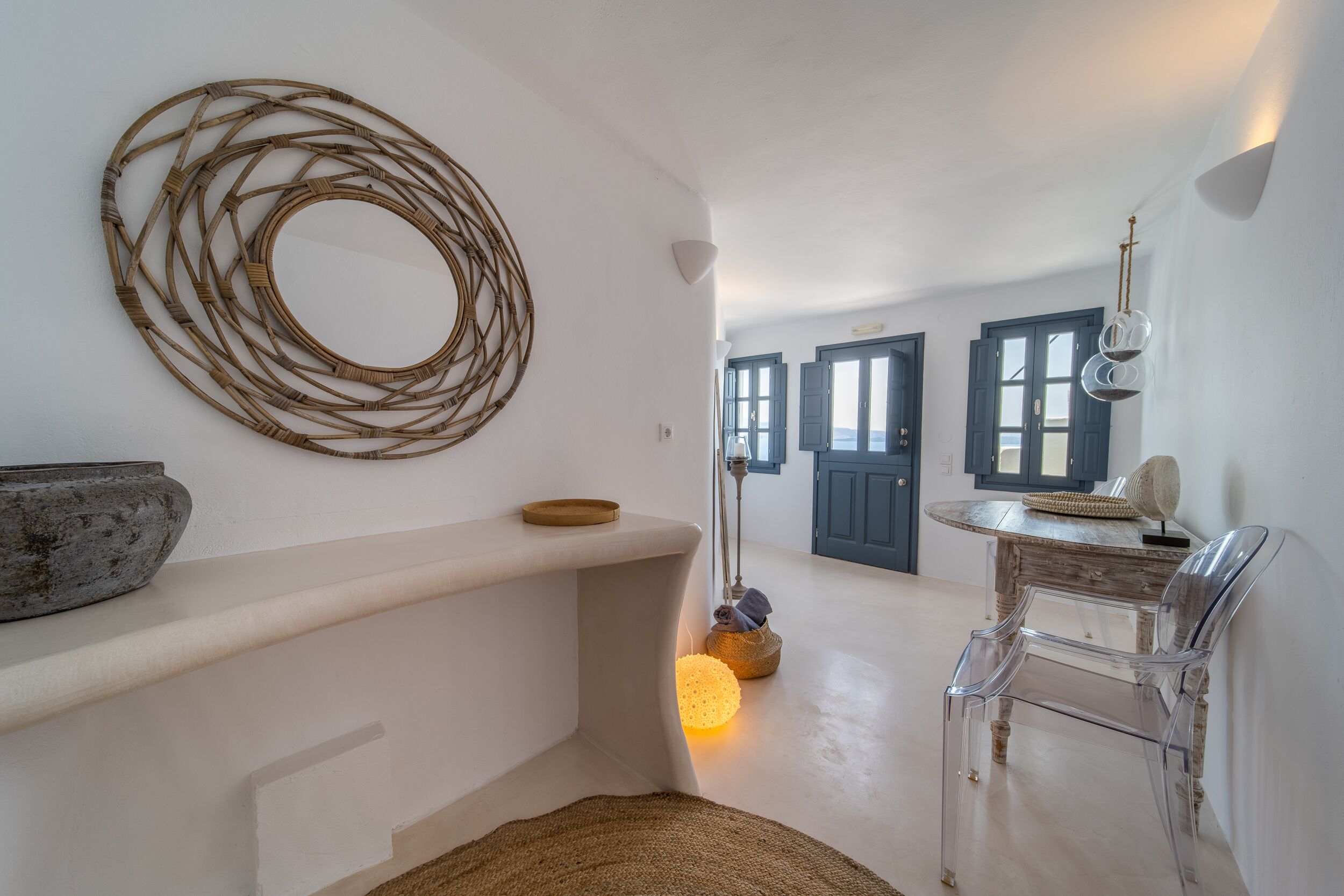 A modern interior with a round woven wall decoration, a rustic bowl, a clear chair, and a lamp with a spherical light.
