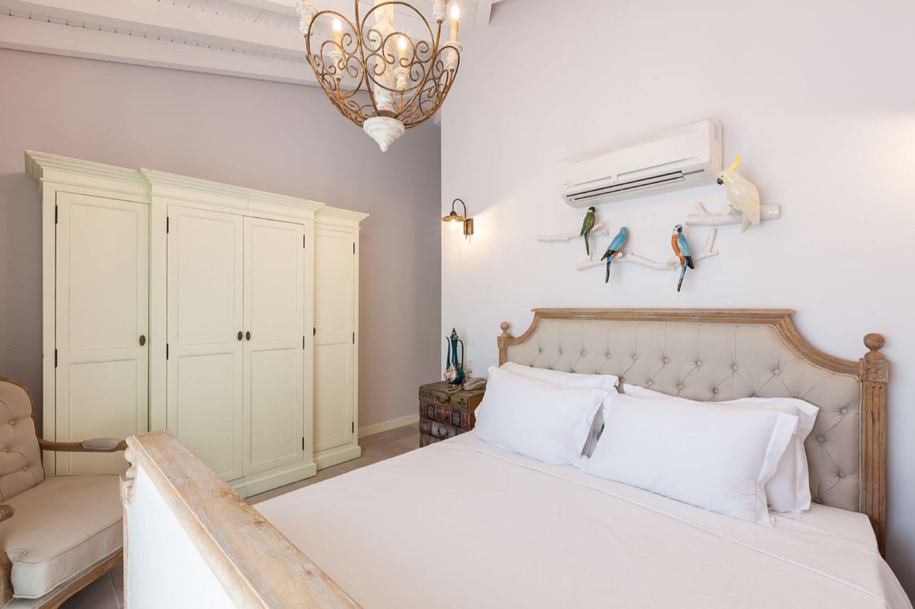 A bedroom with a bed, a chandelier, an air conditioning unit, and wall-mounted bird figurines.