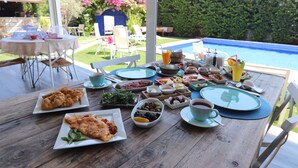 A dining table set with various dishes and drinks, overlooking a pool and garden. - Alacaat Otel (Cesme)
