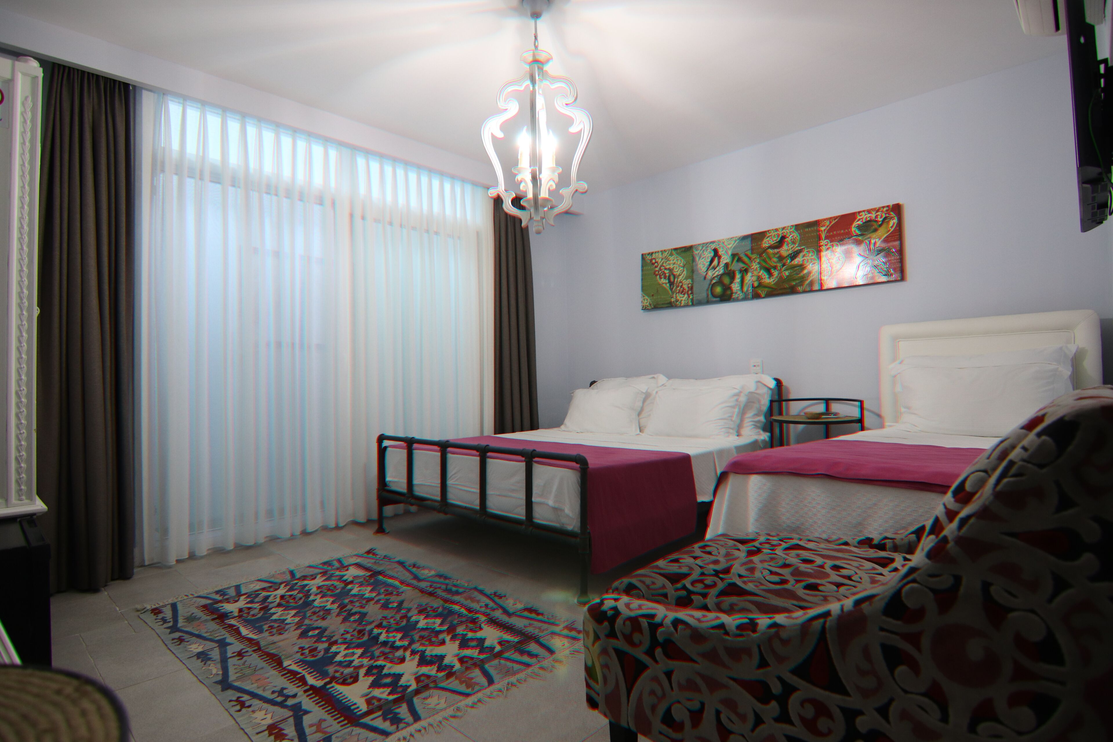 A bedroom with two beds, a chandelier, a patterned rug, and a painting on the wall.