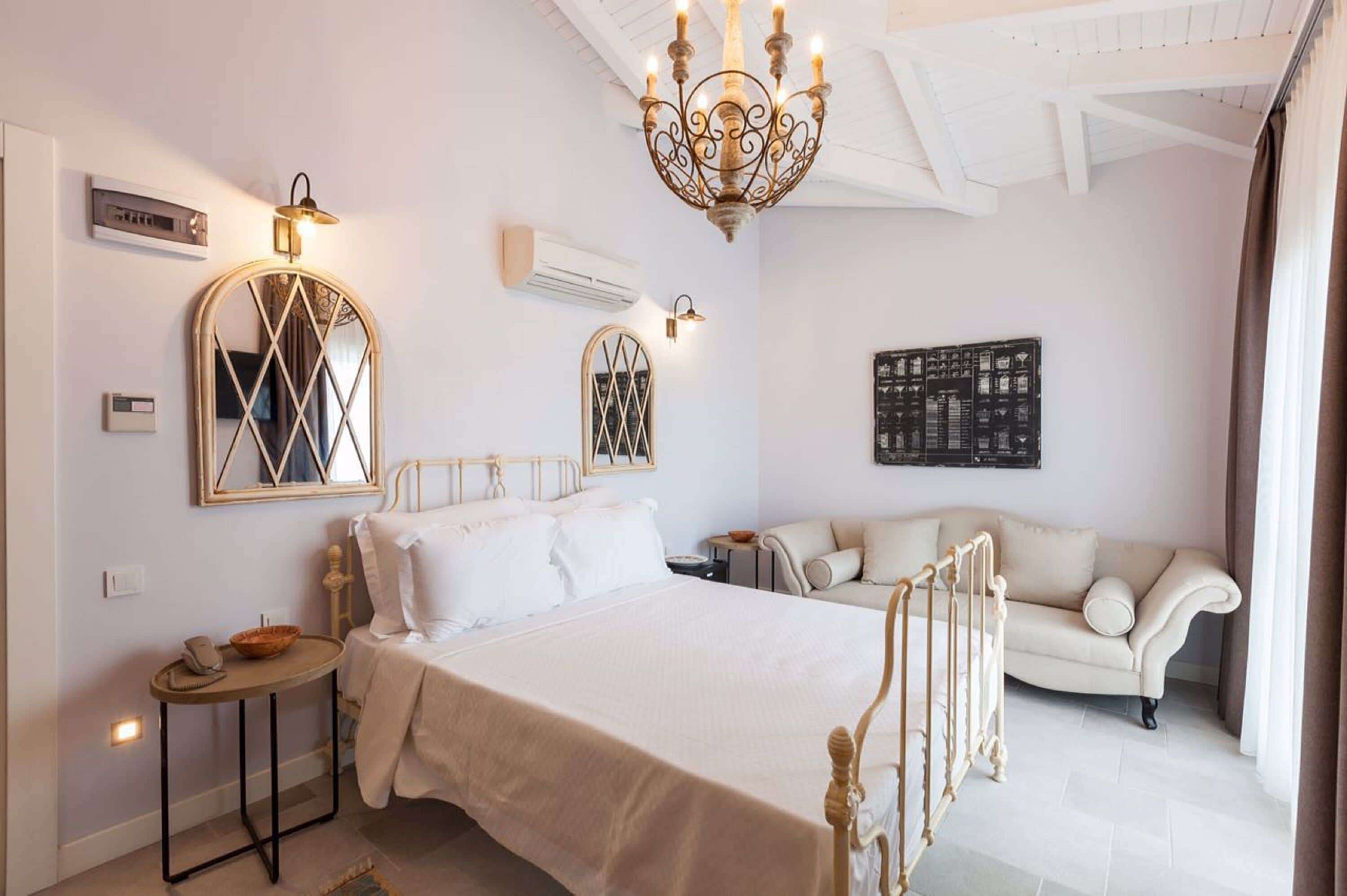 A hotel room with a bed, a sofa, a chandelier, and wall-mounted lights.