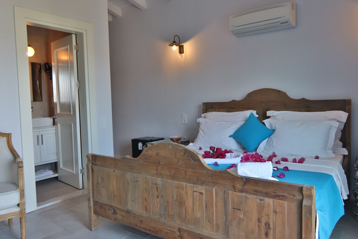 A bedroom with a wooden bed, white linens, a blue pillow, and a wall-mounted light fixture.