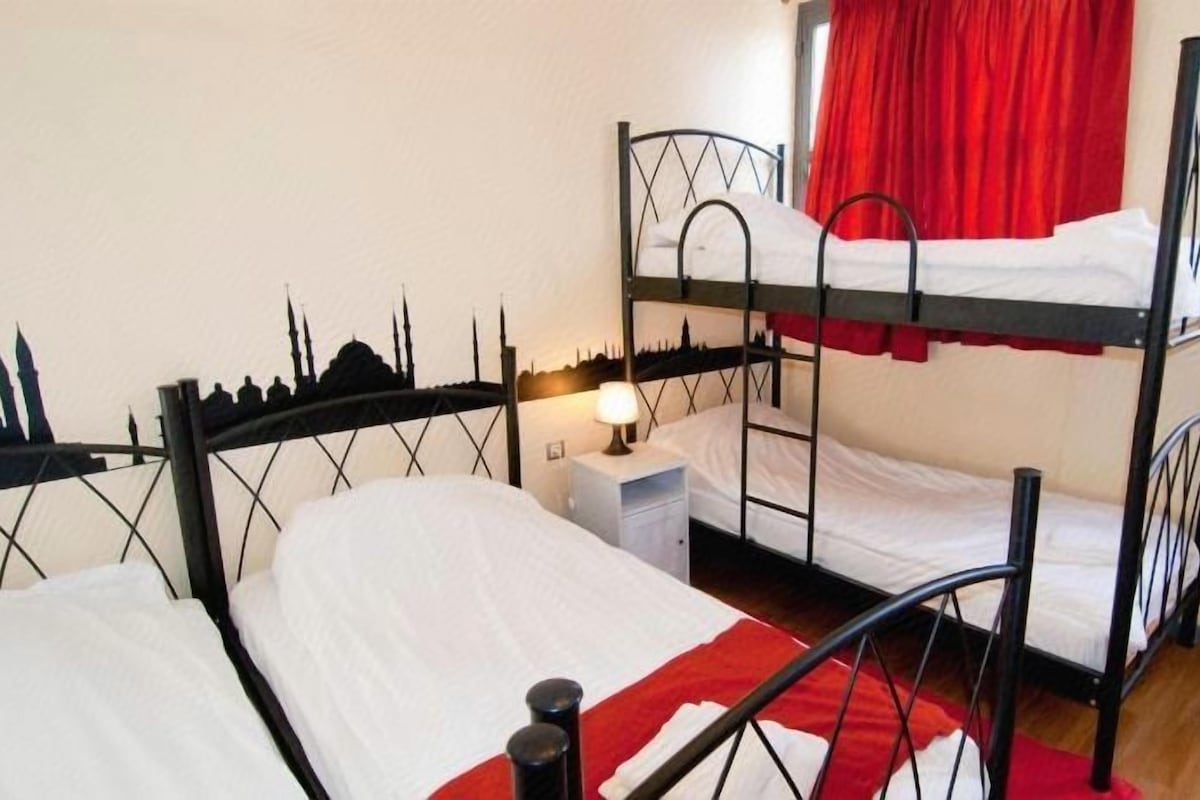 Habitación con literas, silueta del horizonte urbano en la pared, mesita de noche con lámpara y cortinas rojas.