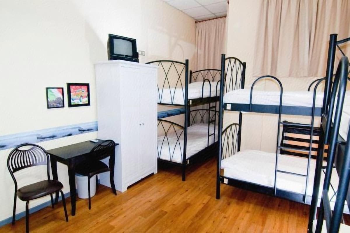 Habitación tipo dormitorio con literas, un escritorio, una silla, un televisor y un refrigerador.