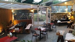 Een terras met tafels en stoelen, een houten bankgedeelte en een koffiehoek.