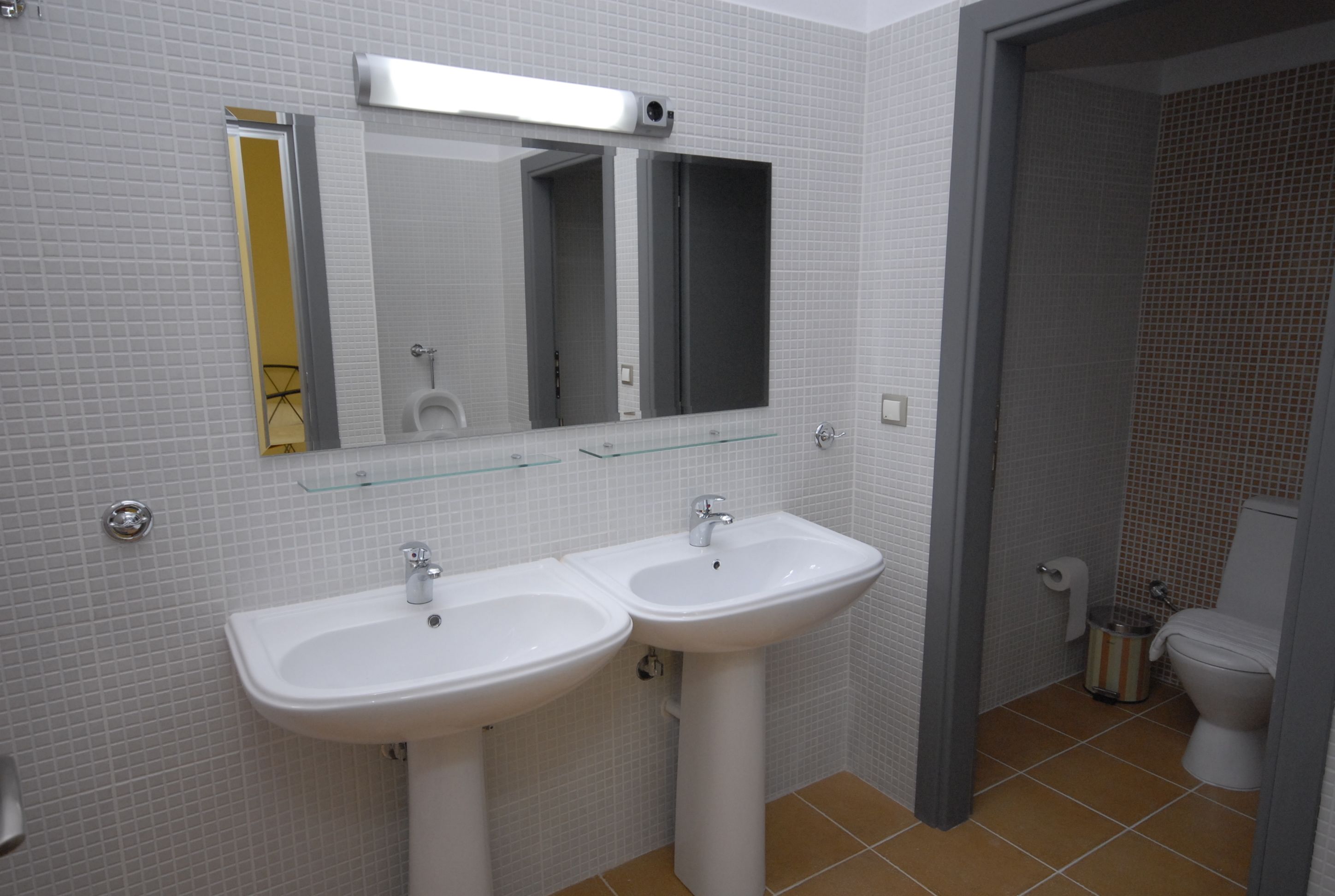 Een badkamer met twee witte wastafels, een spiegel en een toilet.