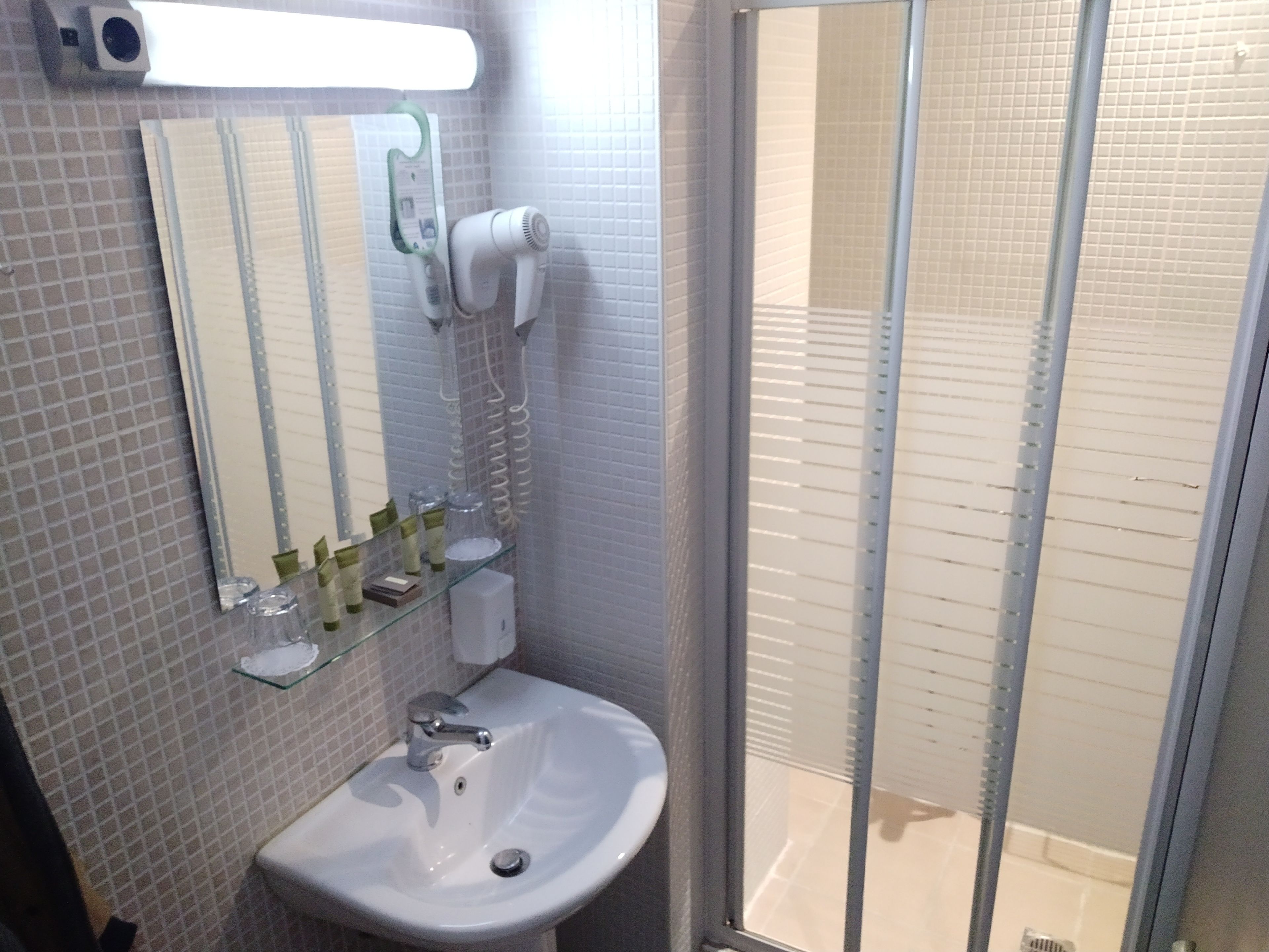 Un baño con lavamanos blanco, espejo y cabina de ducha de vidrio.
