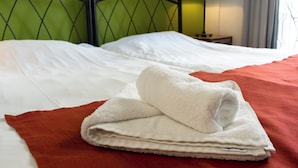 Een opgemaakt bed met witte lakens en een gevouwen witte handdoek op een rode plaid.