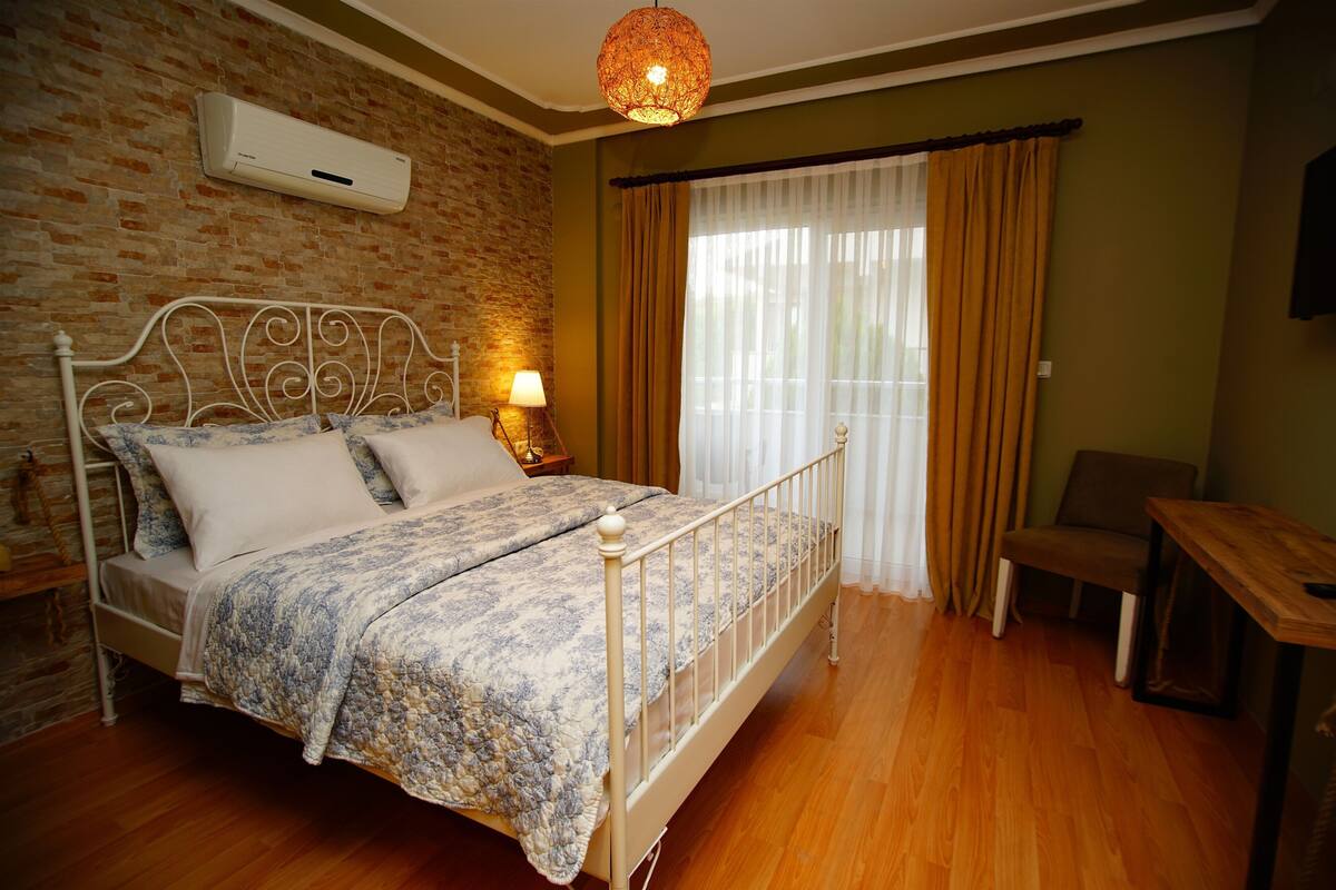 A bedroom with a metal bed frame, a bedside lamp, a wooden table, and a brick wall.