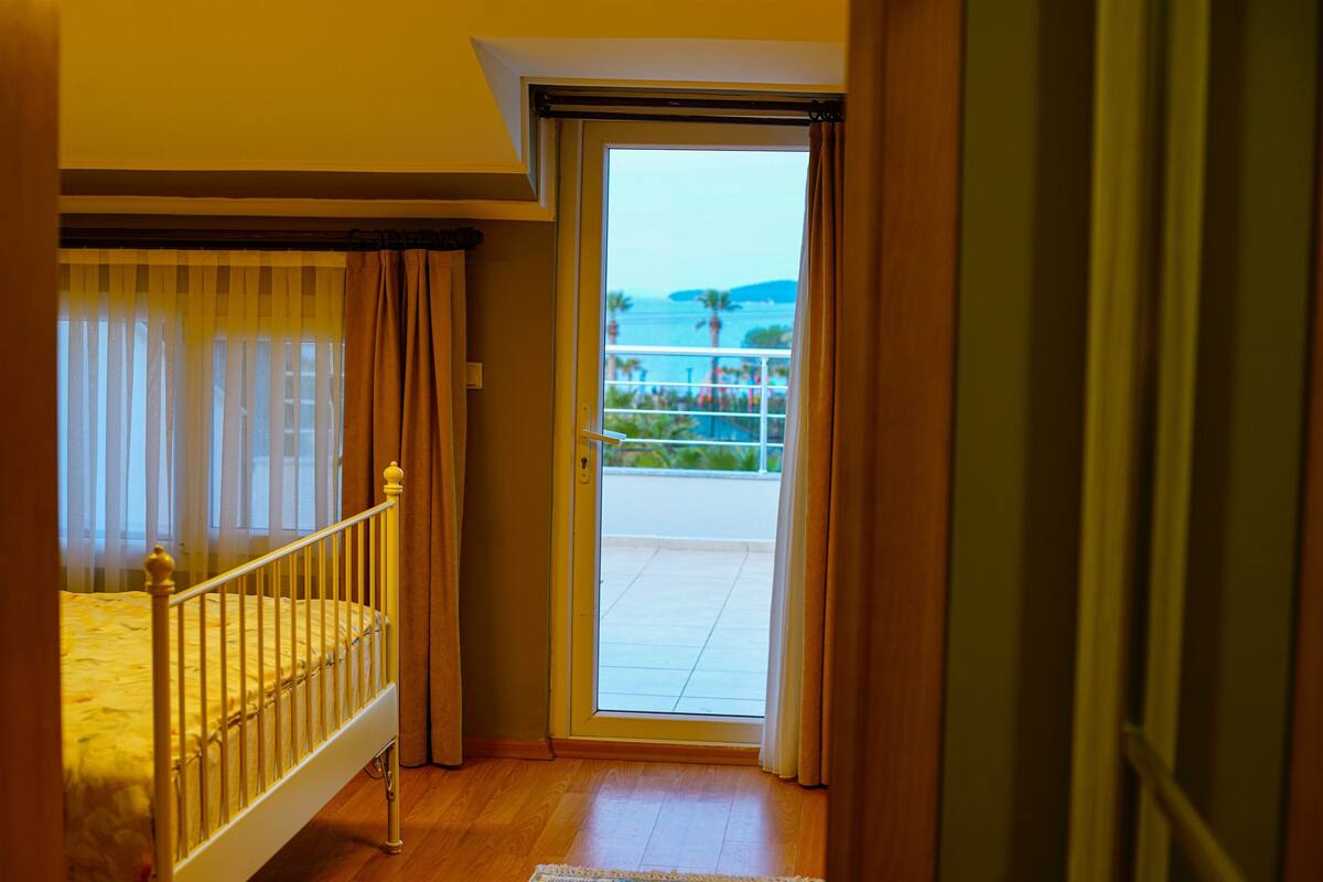 A bedroom with a balcony, wooden flooring, and a bed with a white headboard.