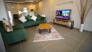 A living room with a green sofa, a wooden coffee table, and a television displaying a news program. - Urla Zeytin Otel (Urla)
