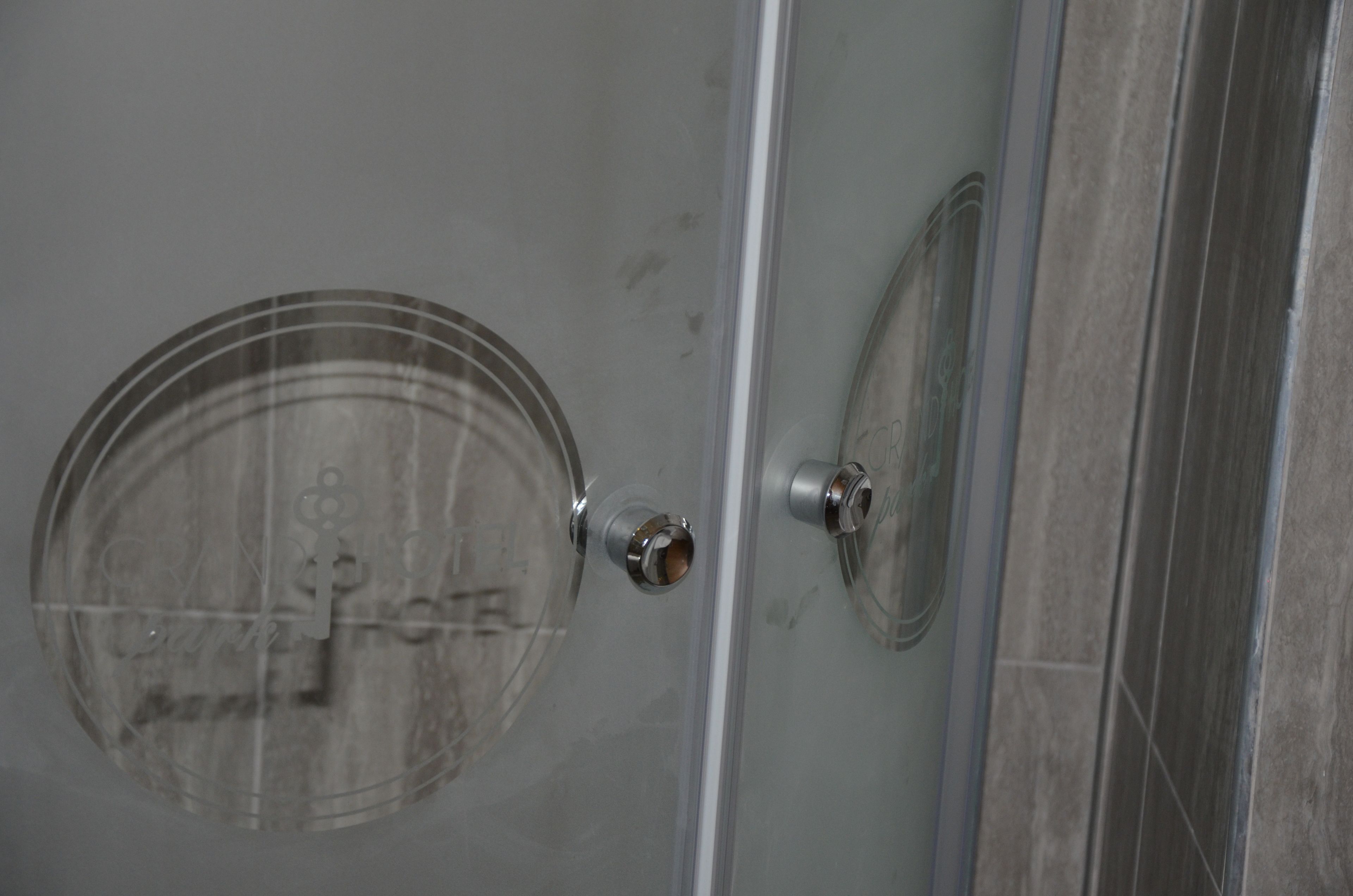 A glass shower door with a circular logo and metallic handles.