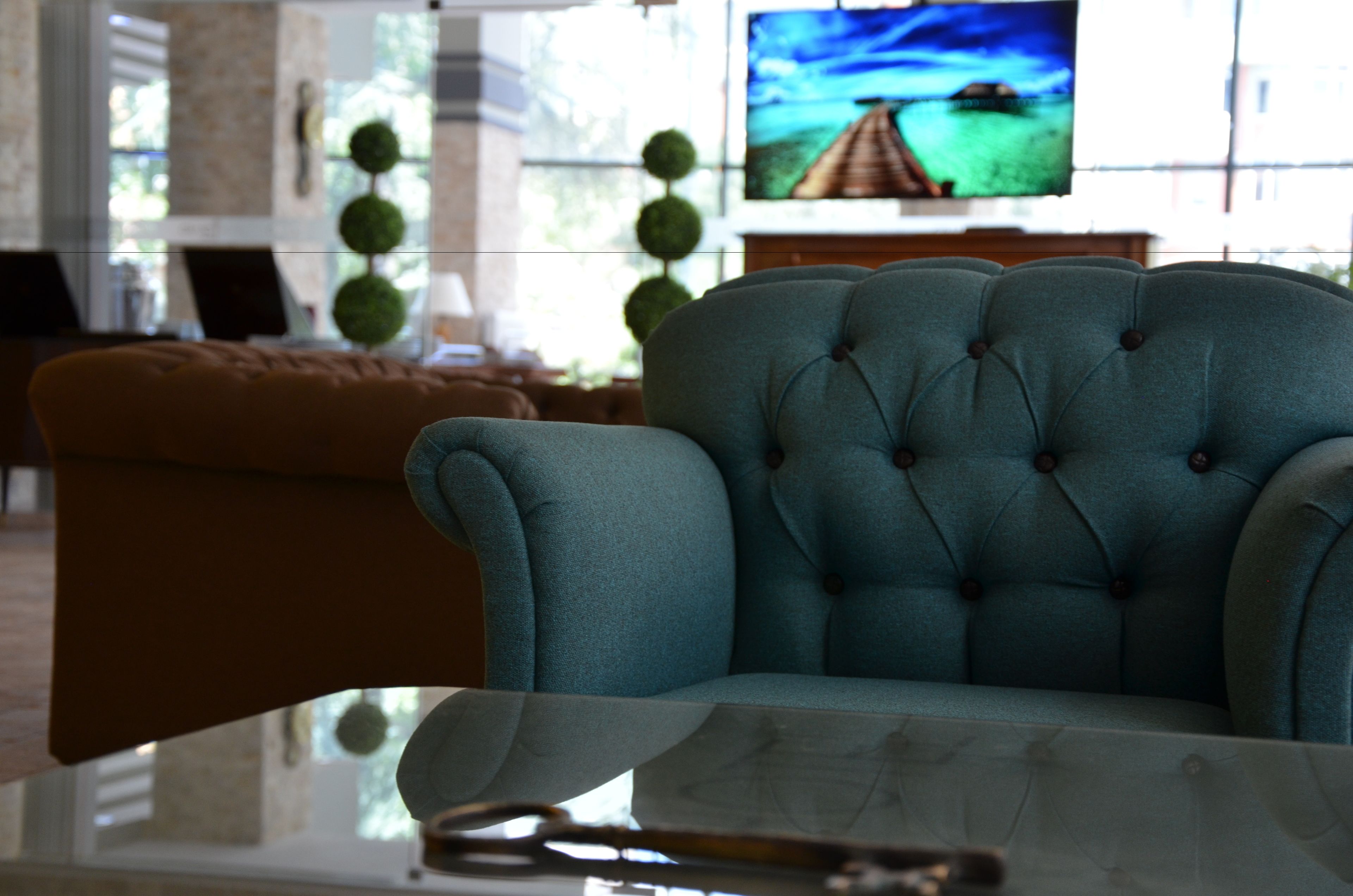 A teal upholstered armchair in a living room with a television displaying a scenic landscape.