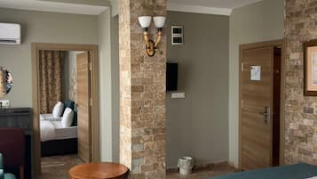 A hotel room with a brick accent wall, a wooden table, a bed with a blue bedspread, a desk with a chair, and a wardrobe.