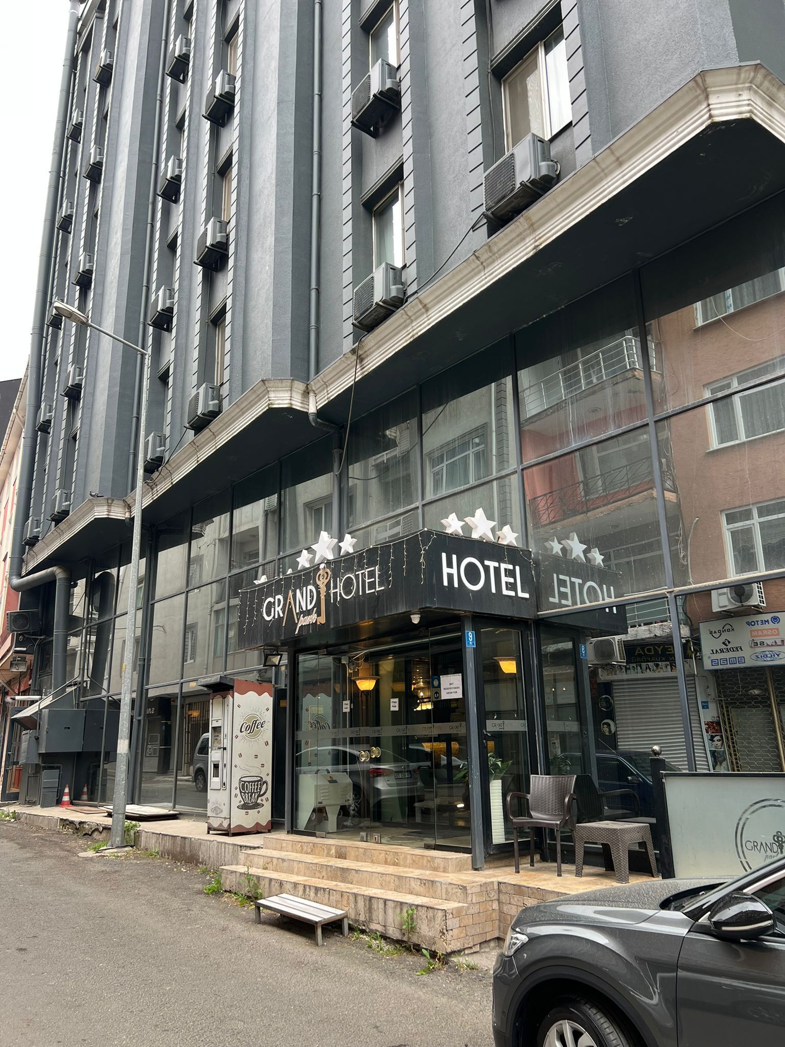 A hotel with a modern facade, large windows, and a visible coffee shop on the ground floor.
