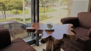 Una habitación moderna con un ventanal grande, una mesa de centro de madera con una taza, y muebles de mimbre.